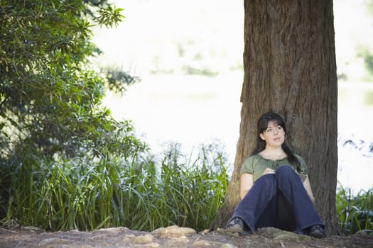 Young Woman sitting by Tree in Woods Writing in Journal