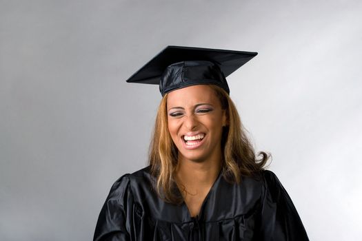 A recent graduate posing in her cap and gown isolated over a silver background.