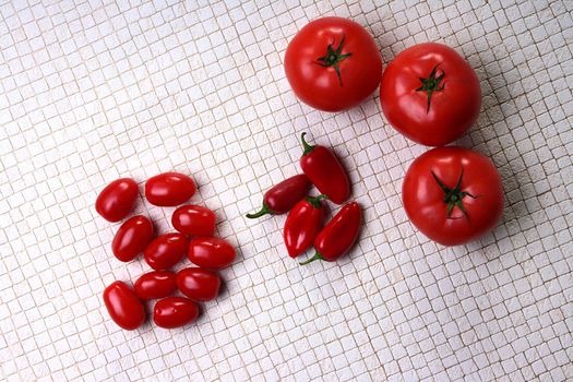 Tomatoes big and small with small hot red peppers on a kitchen table.