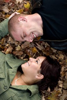 A young happy couple gazing into each others eyes while laying in a pile of leaves.