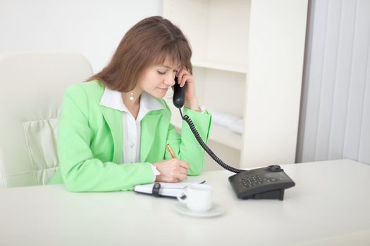 The secretary speaks on the phone doing records in a notebook