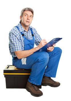 Confident service man sitting on toolbox and taking notes. Isolated on white