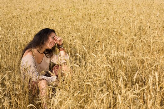 Attractive girl sitting in golden wheat field