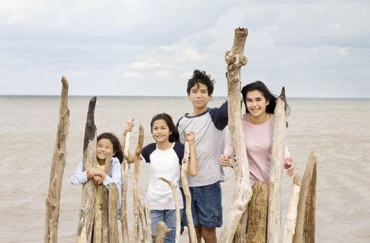 Four siblings by the lakeshore in summer, standing against driftwood fencing