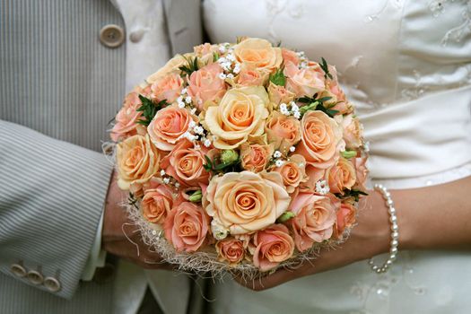 Cream-coloured bouquet in the hands of bride and groom.
