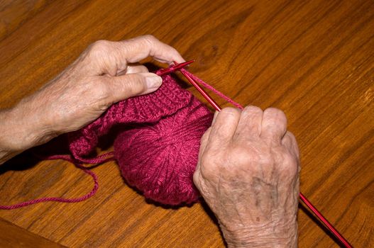 elderly caucasian woman knitting with burgandy wool yarn