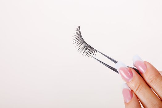 Woman hand holding false eyelashes in pincers