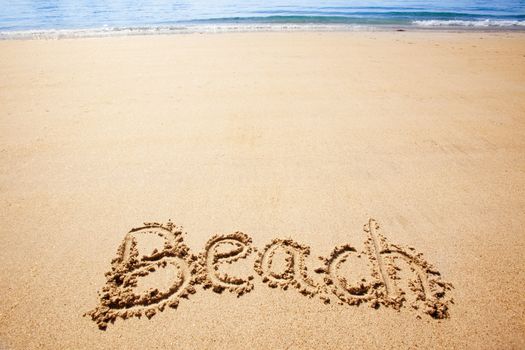 Beach written in the sand on the coast with mountains in the background