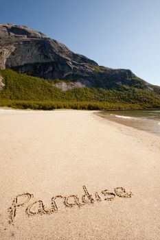 The word paradise written in the sand on a beautiful island