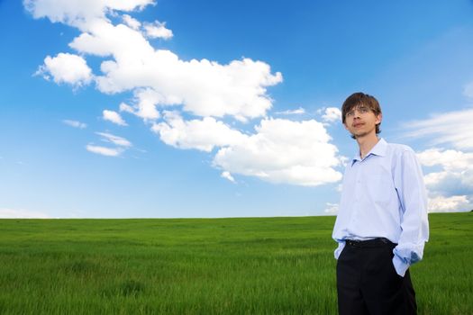Successful businessman standing on green grassland under blue sky