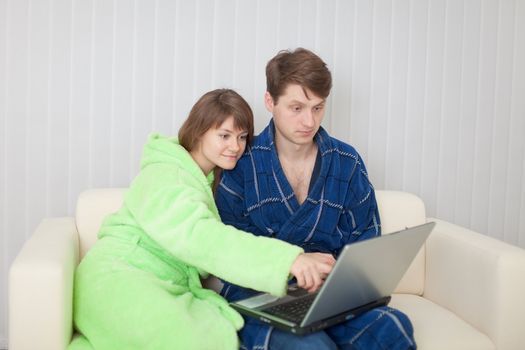 The man and the woman sit on a sofa with the laptop