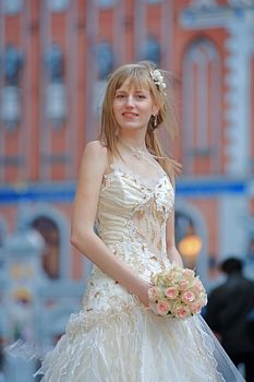 Bride in light dress with cream-colour rose bouquet in her hands and white flowers in her hair.