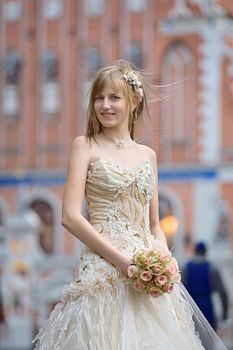 Bride in light dress with cream-colour rose bouquet in her hands and white flowers in her hair.
