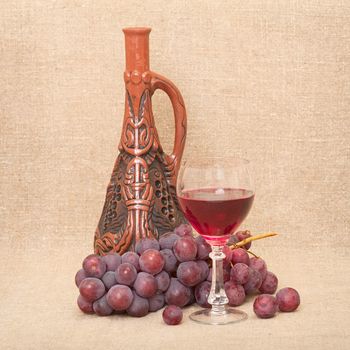 Still-life with a clay bottle, grapes and a glass on a canvas background