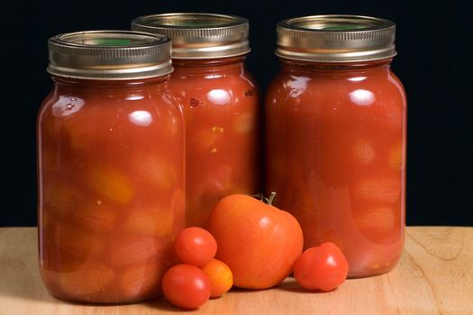 Three mason jars filled with canned tomatoes shot on a wooden board and isolated against a black background