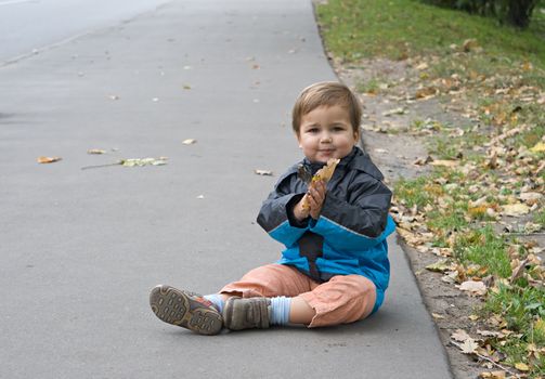 Toddler sitting on the asphalt in autumn