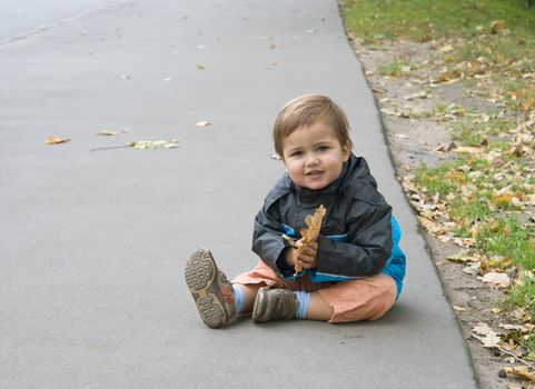 Toddler sitting on the asphalt in autumn