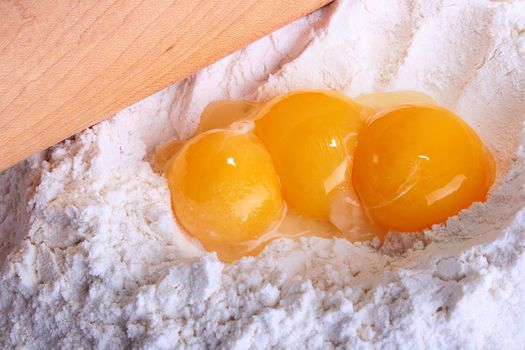 Three egg yolks with rolling pin in a flour. Components for a pie.