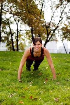 A caucasian female doing push ups in the park