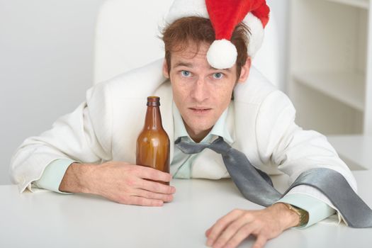 The young man in a Christmas hat at office with a beer bottle