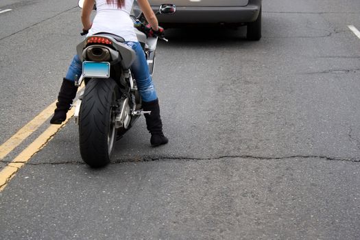 A young woman sitting on a motorcycle stopped in traffic at a red light.