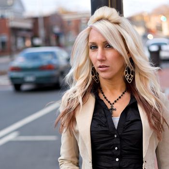 A young blonde woman standing on the side of the road.