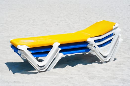 A stack of yellow and blue beach chairs in the sand