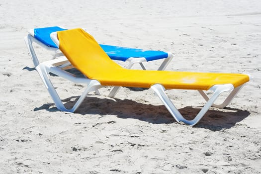 A couple of beach chairs in the sand in a deserted beach