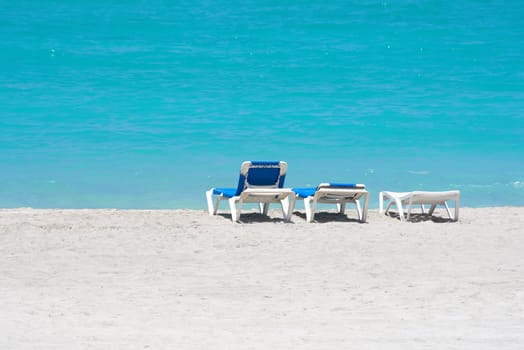 Three beach chairs in a lonely beach with clear blue water
