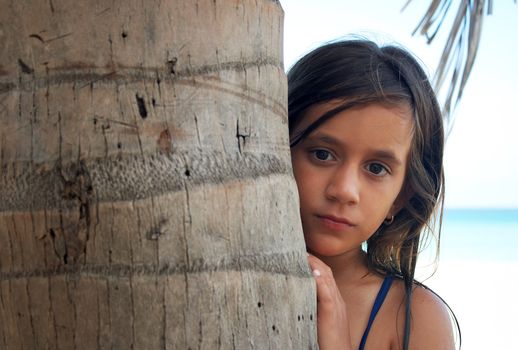 Pretty girl hiding behind a tree in a beautiful beach