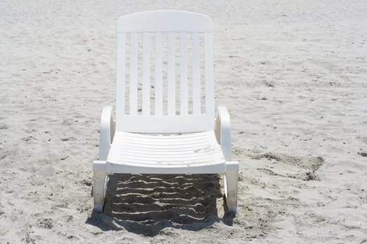 Frontal view of a white plastic chair in a sandy beach