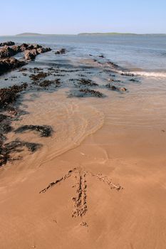arrows giving directions inscribed on the beach with waves in the background on a hot sunny day