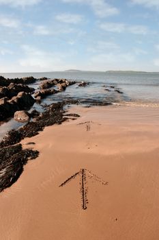 arrows giving directions inscribed on the beach with waves in the background on a hot sunny day