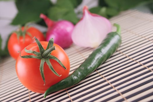 Tomatoes, onions and hot green pepper removed close up on a striped bamboo napkin against green foliage