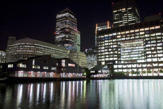 Canary Wharf skyscrapers in London at night with reflections in the river