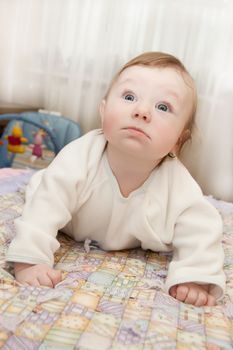 Cute baby boy lying on bed and looking curiously up