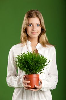 Portrait of a beautiful young woman holding a plant on her hands, isolated on a green background