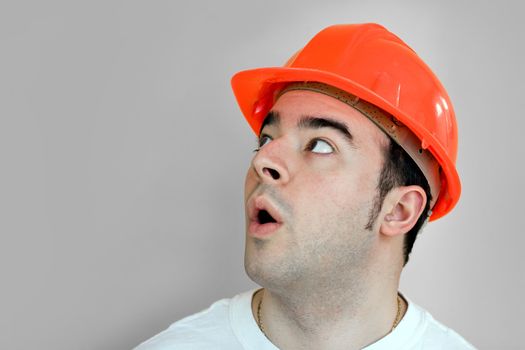 A young construction worker isolated over silver that is looking up at something in amazement.