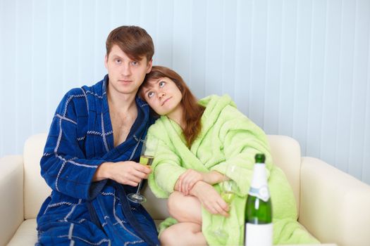 The young pair at home on a sofa with sparkling wine