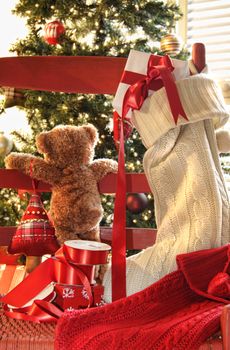 Little teddy bear looking through chair at christmas tree