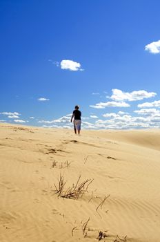 A person is walking alone in the sand dunes