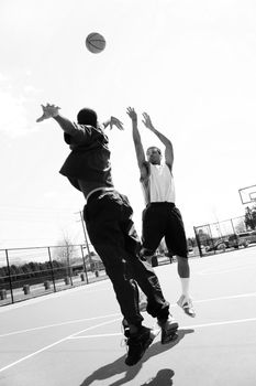 A basketball player shooting the ball at the basket while being guarded by his opponent.