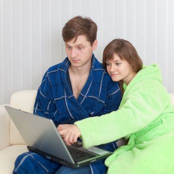 The guy and the woman sit on a sofa with the laptop