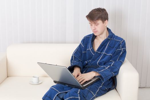 The young man works with the laptop in a blue dressing gown