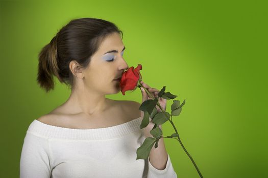 Portrait of a beautiful woman smelling a red rose on a green background