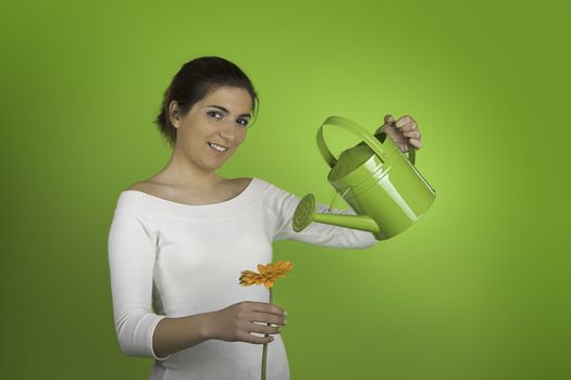 Beautiful woman on a green background watering a gerbera flower