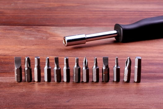 Screw-driver with a set of replaceable nozzles for screws with a different configuration on a wooden table.