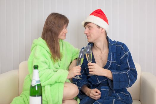 The young couple drinks sparkling wine sitting on a sofa in dressing gowns