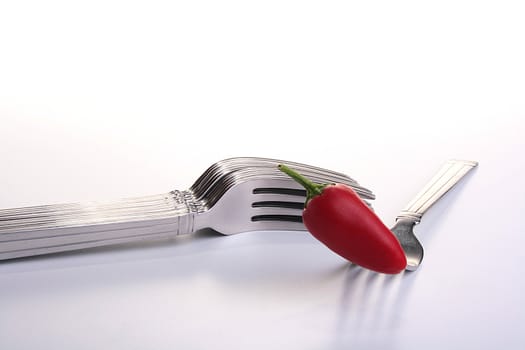 Red hot pepper on fork and a set forks on a background.