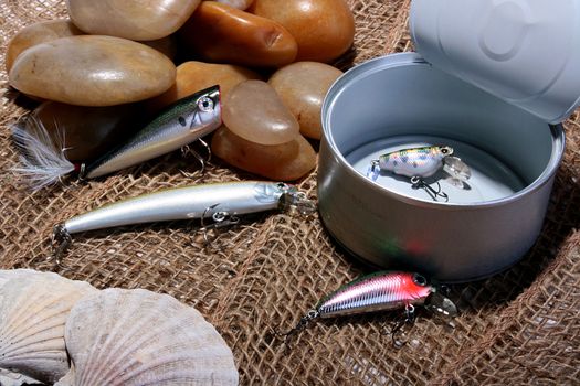 Open can with the spoons hook for fishing. Sea stones and cockleshells against a rough sacking.